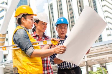 Üç endüstri mühendisi aşınma emniyet kask mühendislik çalışma ve çizimler muayene ile binanın önünde konuşurken. Mühendislik araçları ve inşaat kavramı.