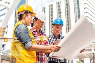 Üç endüstri mühendisi aşınma emniyet kask mühendislik çalışma ve çizimler muayene ile binanın önünde konuşurken. Mühendislik araçları ve inşaat kavramı.