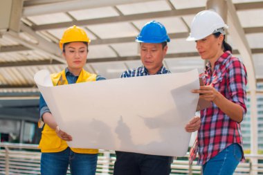 Üç endüstri mühendisi aşınma emniyet kask mühendislik çalışma ve çizimler muayene ile binanın önünde konuşurken. Mühendislik araçları ve inşaat kavramı. Kopya alanı ile