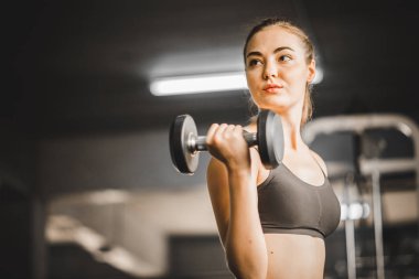 Güzel genç kadın beyaz spor giyim kameraya poz uygun. Bir spor salonunda bir egzersiz dersi sırasında halter tutan genç kadın. Sağlıklı spor yaşam tarzı, Fitness kavramı.