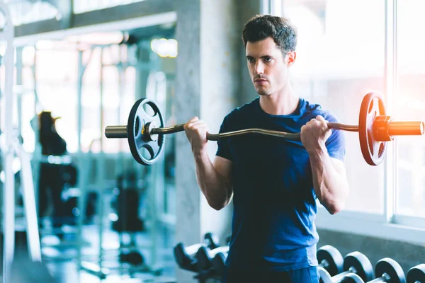 Beyaz yakışıklı genç ve büyük kas spor içinde uygun. Genç adam bir spor salonunda bir egzersiz dersi sırasında dumbbell tutarak. Sağlıklı spor yaşam tarzı, Fitness kavramı.
