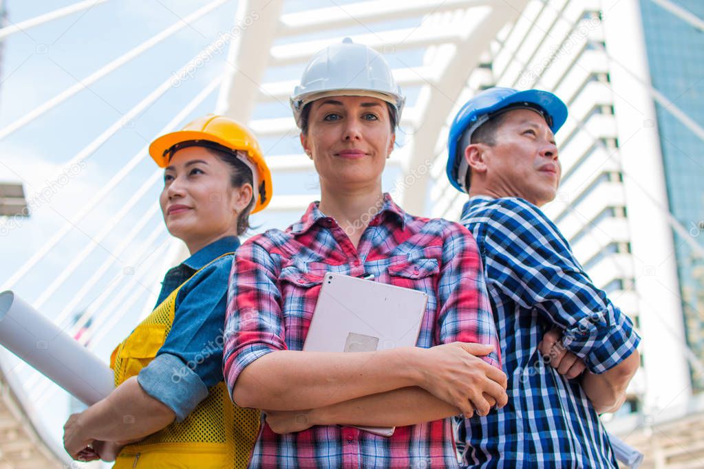 Three Industrial engineer wear safety helmet engineering standing with arms crossed on building outside. Engineering tools and construction concept.