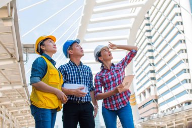 Üç endüstri mühendisi giyim kask ve Mühendislik çalışma ve çizimler muayene ile binanın önünde konuşurken holding tablet. Mühendislik araçları ve inşaat kavramı. Kopya alanı ile