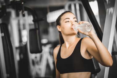 Genç kadın beyaz oturma ve egzersiz yaptıktan sonra dinlenme uygun ya da fitness salonunda egzersiz. kadın bir mola spor salonunda ve spor giyim suda rahatlayın. Fitness kavramı, sağlıklı, spor, yaşam biçimi