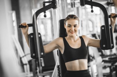 Güzel genç kadın egzersiz egzersiz jimnastik salonu makinedeki uygun. Memnun gülümseyen kız onu eğitim süreci ile keyfini çıkarın. Fitness, sağlıklı, spor, yaşam kavramı