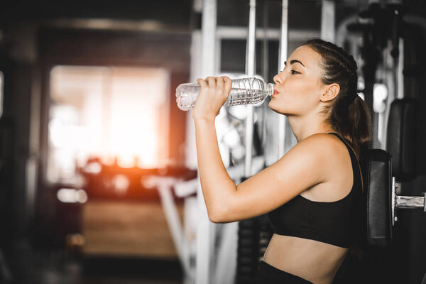 Fit young woman caucasian sitting and resting after workout or exercise in fitness gym. woman at gym taking a break and relax with water in sportswear. Fitness concept, Healthy, Sport, Lifestyle