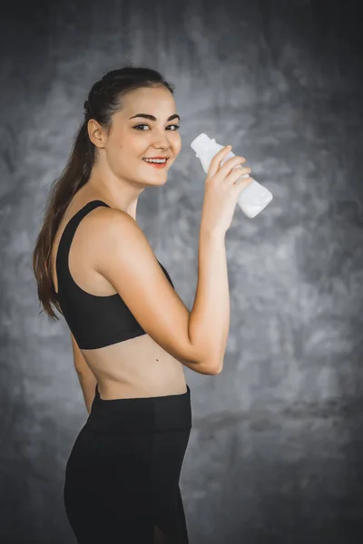 Fit young woman standing and drinking milk in bottle after workout or exercise in gym. Woman at gym taking a break and relax with milk in sportswear. Fitness concept, Healthy, Sport, Lifestyle