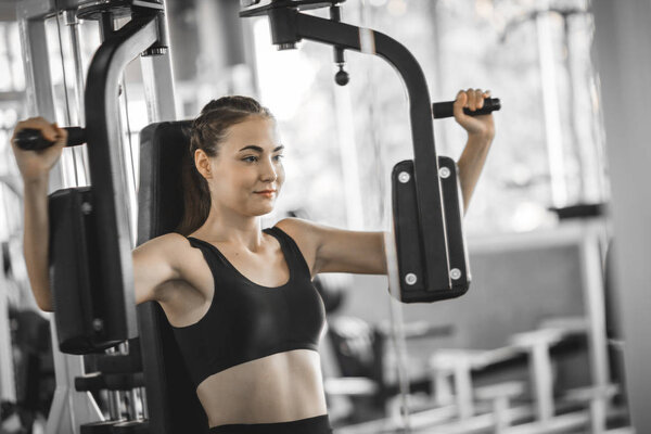 Fit beautiful young woman exercise workout on machine in gym. Glad smiling girl is enjoy with her training process. Concept of fitness, Healthy, Sport, Lifestyle