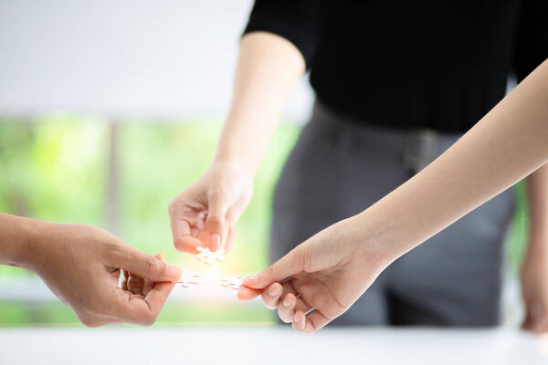 Business teamwork, partnership and brainstorm concept. Group of business people assembling jigsaw puzzle pieces together on desk table.