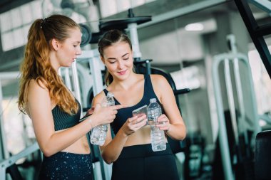 Güzel genç kadın sporcular spor olarak çalışma sonra fitness giysilerle rahatlatıcı uygun. Şişe suda Holding ayakta ve fitness app smartphone kullanarak iki kadın. Spor, yaşam kavramı, sağlıklı.