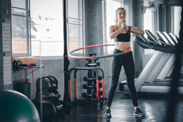 Güzel beyaz genç kadının adım bel ileriye doğru duruş doldurma hula hoop yapması. Genç kadın bir spor salonunda bir egzersiz dersi sırasında hula hoop yapıyor. Sağlıklı spor yaşam tarzı, Fitness, sağlıklı kavramı.