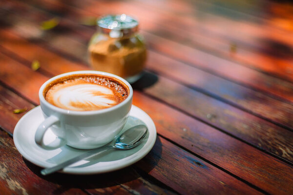 Hot coffee latte cappuccino spiral foam on wooden table in coffee shop cafe with vintage color tone filter background. With copy space for your text. Color tone effect