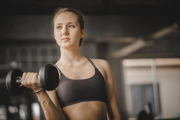 Fit beautiful young woman caucasian posing at the camera in sportswear. Young woman holding dumbbell during an exercise class in a gym. Healthy sports lifestyle, Fitness concept.
