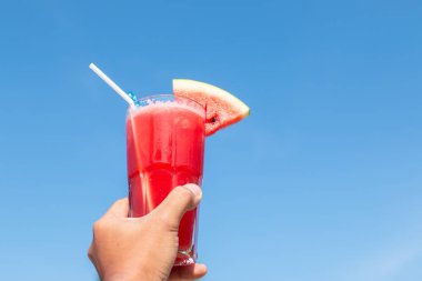 Sağlıklı kavram, el ele tutuşan karpuz suyu ve mavi gökyüzü arka planı..