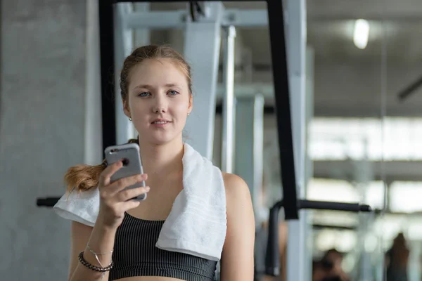Genç ve çekici kadınlar spor salonunda spor yaparken akıllı telefon kullanıyor. Spor salonunda sıkı çalıştıktan sonra rahatlama. Sağlıklı spor yaşam tarzı, spor konsepti.