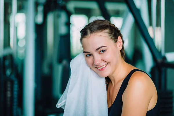 Junge attraktive Frau kaukasischen sitzt und mit Handtuch den Schweiß abwischen. Entspannung nach hartem Training im Fitnessstudio. Fitnesskonzept, gesund, Sport, Lebensstil — Stockfoto