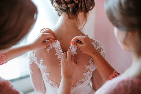 La dama de honor ayuda a sujetar un vestido de novia la novia antes de la ceremonia. Vestido de novia de lujo de cerca. La mejor mañana. Concepto de boda — Foto de Stock