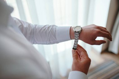 Beyaz gömlekli bir adam bir saat kolunda giyer.