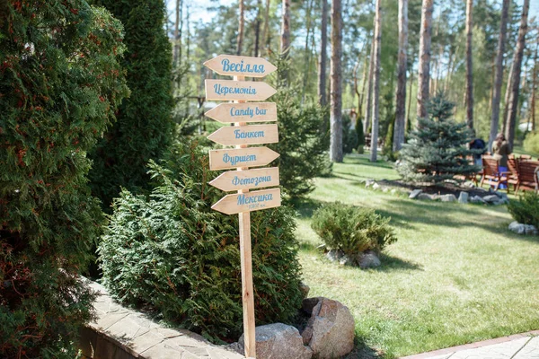 The close-up photo of the wooden plaque with the signs Welcome to the wedding standing in the street on a green banquet background. wedding decor