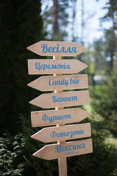 The close-up photo of the wooden plaque with the signs Welcome to the wedding standing in the street on a green banquet background. wedding decor