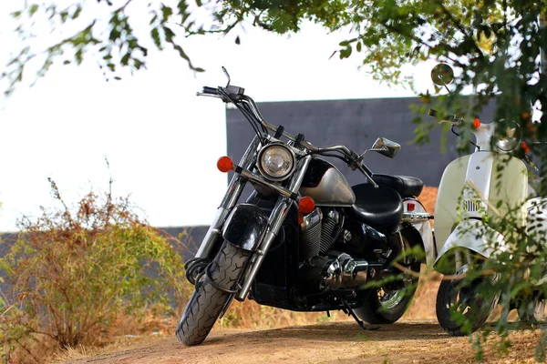 Beyaz motosikletin yanında duran klasik siyah motosiklet güneş ışığının altında. Yan görünüm