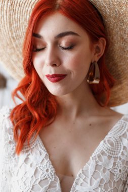 Düğün içeriği - yakın çekim Bir dekorasyon ile beyaz bir arka plan üzerinde bir sandalyede oturan bir stüdyoda bir şapka genç güzel kızıl saçlı kız Portresi. Kopyalama alanı