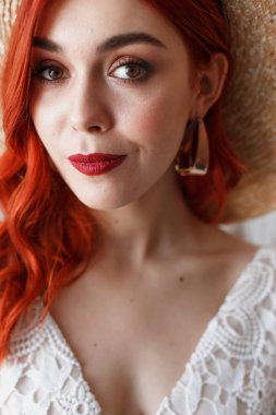 Düğün içeriği - yakın çekim Bir dekorasyon ile beyaz bir arka plan üzerinde bir sandalyede oturan bir stüdyoda bir şapka genç güzel kızıl saçlı kız Portresi. Kopyalama alanı