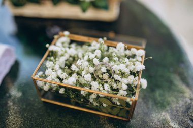 Altın alyanslar beyaz çiçeklerle dolu cam bir kutuda