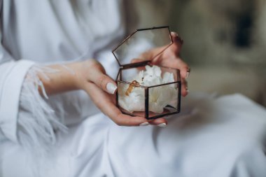 Gelin ve damadın alyansları cam bir kutunun içinde sulu sularda, kutu da gelinin ellerinde.