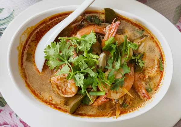 Tom yam kung, the traditional Thai sour soup with prawns and champignons, topped with coriander. The photo shows the red version of the soup, made with coconut milk, also called tom yam kathi. Shallow depth of field.