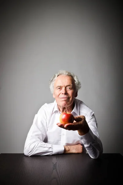 Old man in white is sitting and holding an apple.