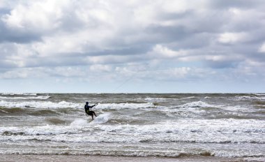 Kitesurfer Baltık Denizi dalgalar bulutlu gökyüzü altında Venspils beach yakınındaki biniyor. Eğlenceli denizin içinde. Aşırı spor kitesurfing.