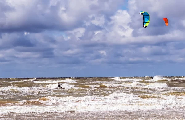 İki kitesurfers Baltık Denizi dalgalar bulutlu gökyüzü altında Venspils beach yakınındaki biniyor. Eğlenceli denizin içinde. Aşırı spor kitesurfing.