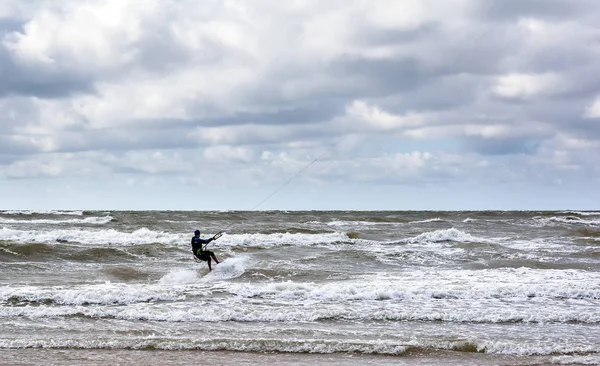 Kitesurfer Baltık Denizi dalgalar bulutlu gökyüzü altında Venspils beach yakınındaki biniyor. Eğlenceli denizin içinde. Aşırı spor kitesurfing.