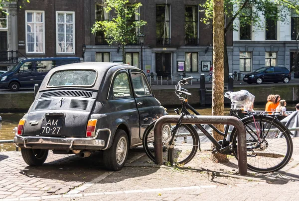 Amsterdam, Hollanda - 21 Mayıs 2018: bisiklet yakınındaki Amsterdam kanalları birinde eski paslı İtalyan küçük araba Fiat 500 l veya Lusso Park siyah arka.