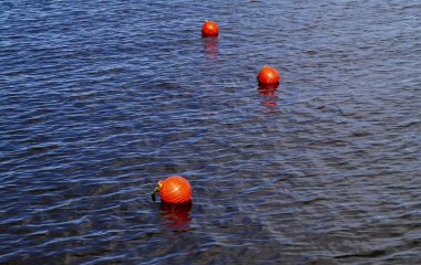 Three bright orange buoys floating on river water surface. Set of three orange safety buoys in a river with small waves on water surface.