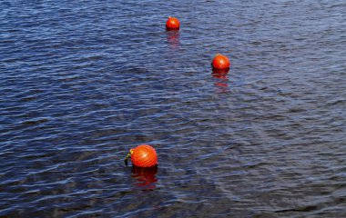 Three bright orange buoys floating on river water surface. Set of three orange safety buoys in a river with small waves on water surface. clipart