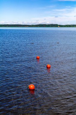 Three bright orange buoys floating on river water surface with woods at the horizon. Set of three orange safety buoys stretching into the distance.