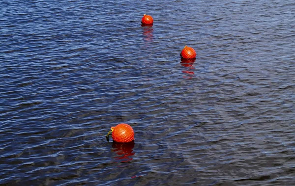 Three bright orange buoys floating on river water surface. Set of three orange safety buoys in a river with small waves on water surface.