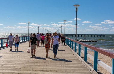 Palanga rıhtımında yürüyen insanlar güneşli havanın tadını çıkarıyorlar. En popüler Palanga yerlerinden biridir ve genellikle Palanga Köprüsü olarak adlandırılır..