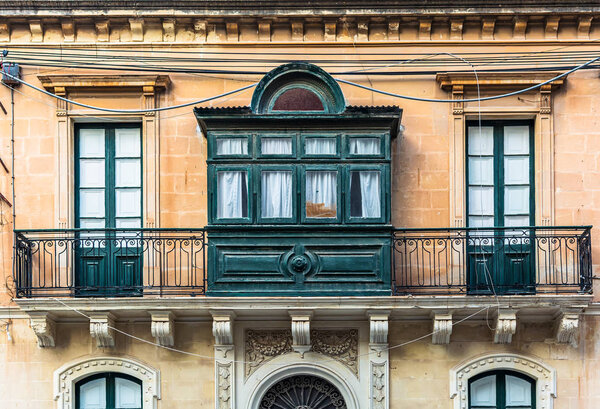 Residential house facade with traditional Maltese wooden balcony in Sliema, Malta, coloured in orange with evening sunlight. Authentic Maltese urban scene.