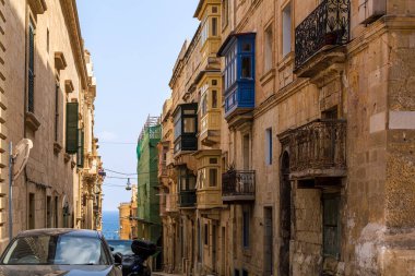 Malta 'nın Valletta kentindeki geleneksel çok renkli ahşap balkonlu, arka planda deniz bulunan ev cephesi. Otantik Malta şehir sahnesi.