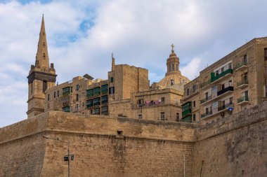 Valletta tahkimat duvarı ve feribot limanından çekilen ünlü binalar. St. Paul 's Anglikan Katedrali' nin kulesi ve Carmelite Kilisesi 'nin tepesi mavi gökyüzüne karşı..