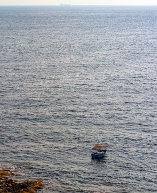 Yalnız tekne Akdeniz 'de, Malta' nın Sliema kıyı şeridi yakınlarında yüzüyor. Balıkçı teknesi, Sliema kıyısı yakınlarındaki açık denizde demirli ve sıcak yaz akşamında kumtaşı plajında..