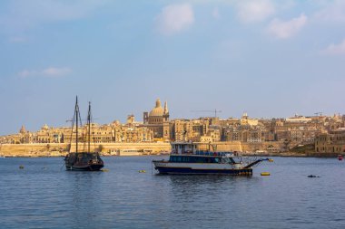 Güneşli yaz gününde Valletta 'nın kıyı manzarasında, modern tekne ve ortaçağ gemisi ön planda. Malta Valletta silueti Carmel Dağı 'nın Leydisi ve St. Paul Katedrali' nin Kilisesi ile birlikte..