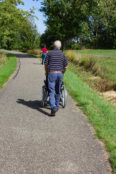 Äldre Man Med Rullstol Och Damen Med Kryckor Promenader Bikeway — Stockfoto