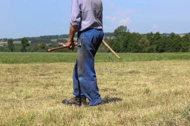 Haziran ayında Güney Almanya çok güneşli bir günde saman, araçları ve mavi pantolon gün sona ermeden işi için çalışkan çiftçi haying görüşürüz