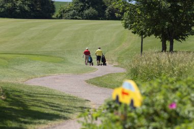 çok güneşli bir Güney Almanya'da golf çim yeşil gördüğünüz ve bayrak ve oyuncular ve kum alanları ve golfplace çevresinde yolu olan mahkeme