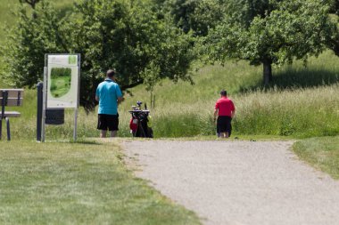 çok güneşli bir Güney Almanya'da golf çim yeşil gördüğünüz ve bayrak ve oyuncular ve kum alanları ve golfplace çevresinde yolu olan mahkeme