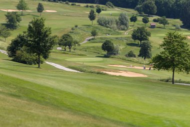 çok güneşli bir Güney Almanya'da golf çim yeşil gördüğünüz ve bayrak ve oyuncular ve kum alanları ve golfplace çevresinde yolu olan mahkeme